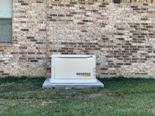 Generac generator installed on a concrete pad against a brick wall