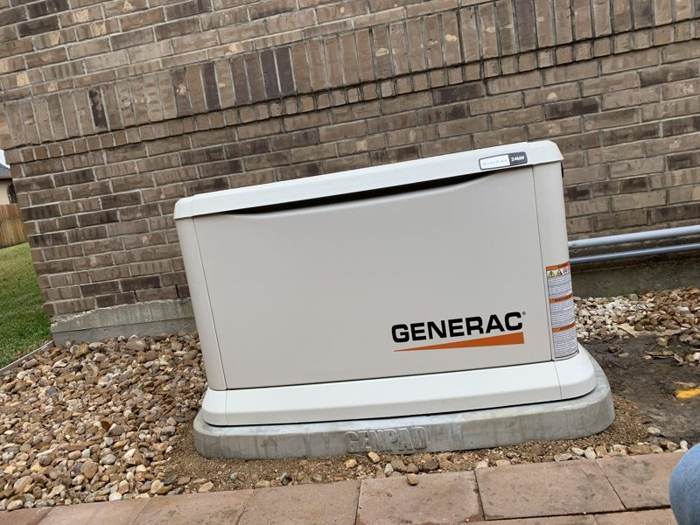 Generac generator on a rock bed beside a brick home